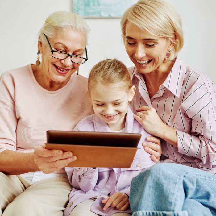 Portrait of happy all women family looking at digital tablet screen and smiling while sitting on couch together